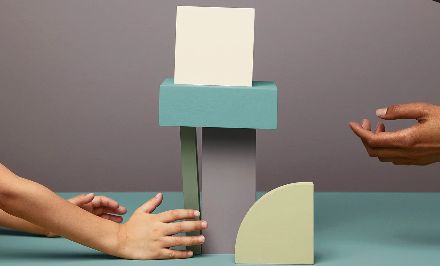 Two pairs of hands playing with painted elements, stocking them on top of each other. 